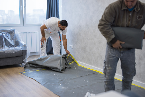Man finishing with wall painting and removing protective nylon from the floor