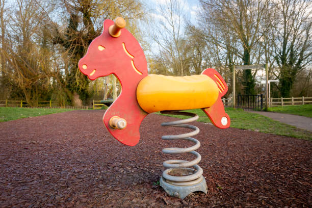 Colourful children's rocking horse on springs over wood chip floor in outdoor playground with trees. Colourful red and yellow children's rocking horse on springs over wood chip floor in outdoor playground with trees. Fun see saw activity game for kids. game swing stock pictures, royalty-free photos & images
