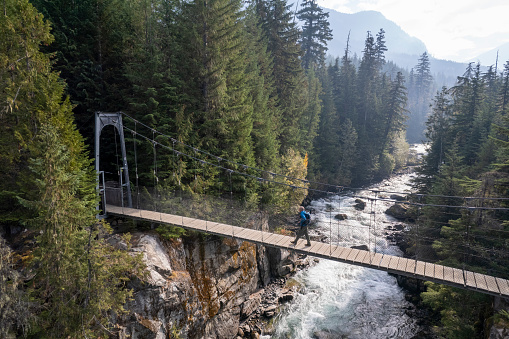 Man hiking on a suspension bridge over a river in a lush forest. Nature, environment and sustainability concepts.