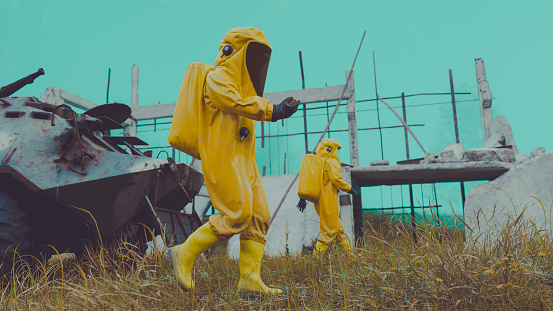 Workers wear yellow hazmat suits to protect them from radiation or a virus. They walk in a dangerous area that has been contaminated.