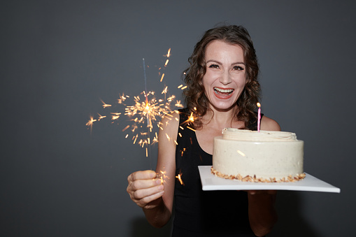 Portrait of happy mature woman with birthday cake and burning bengal light