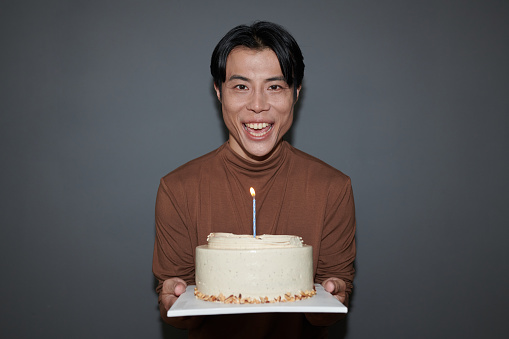 Portrait of happy man holding birthday cake with one candle