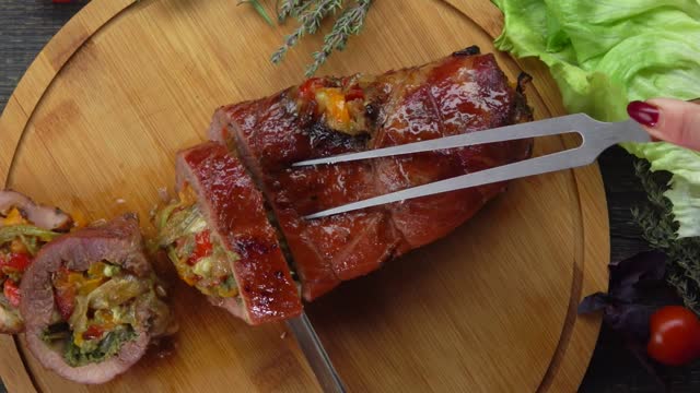 Knife cuts a piece from appetizing juicy baked pork stuffed with vegetables