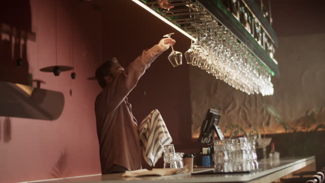 Male bartender wiping glass with towel and hanging it over counter