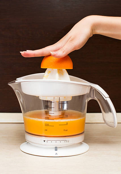 Woman squeezes an orange juice in kitchen stock photo