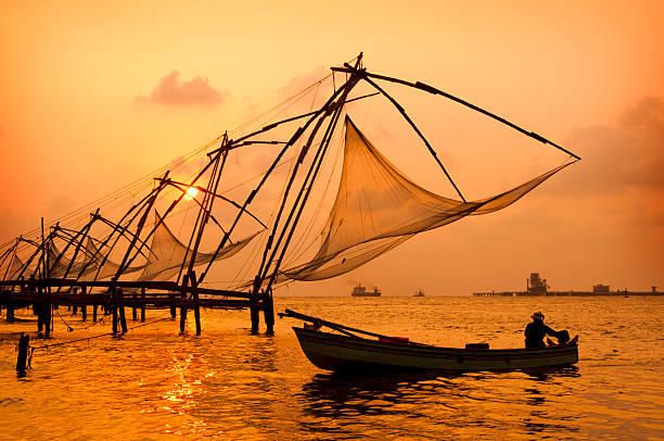 A sunset over Chinese fishing nets by a canoe in Cochin Sunset over Chinese Fishing nets and boat in Cochin (Kochi), Kerala, India.Sunset over Chinese Fishing nets and boat in Cochin (Kochi), Kerala, India.Sunset over Chinese Fishing nets and boat in Cochin (Kochi), Kerala, India. kochi india stock pictures, royalty-free photos & images