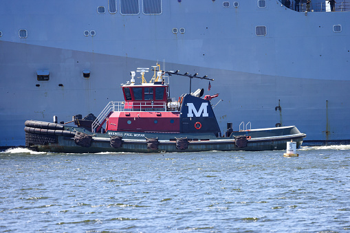 Norfolk, Virginia, USA - April 18, 2023: The Tug Boat Maxwell Paul Moran escorting a Navy vessel up the Elizabeth River in Norfolk.