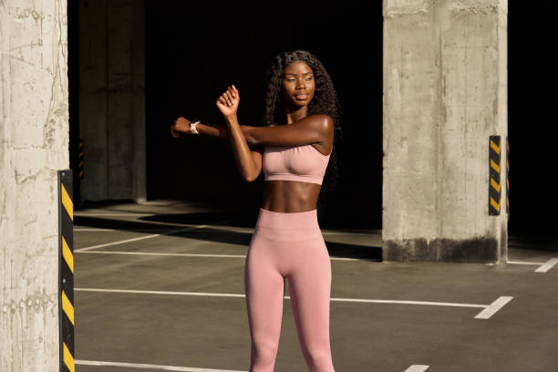 Young fit African woman model doing warming up exercise standing outdoors.