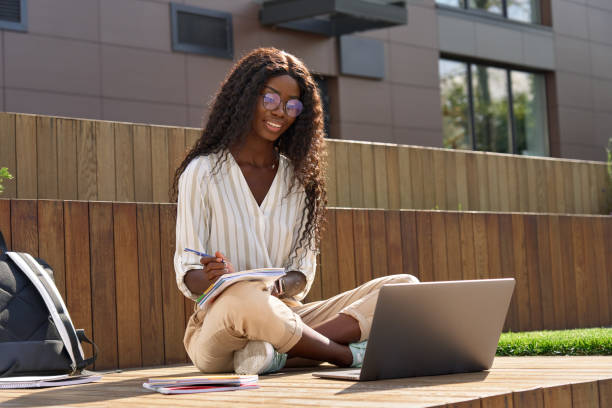 istock Happy black young woman student learning looking at laptop outside campus. 1484245467