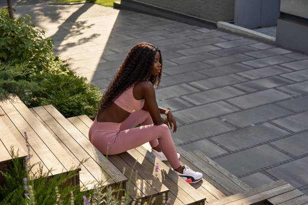 Young fit African woman model sitting in city park relaxing outdoors.