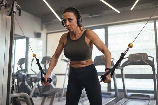 Strong, fit woman using cables for a workout on the crossover machine at the gym