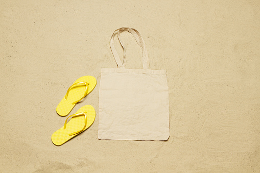 Mockup shopper handbag beach sand background. Top view copy space shopping eco reusable bag. Flip flops accessories. Template blank top view white cotton material canvas cloth. Empty mock-up beach