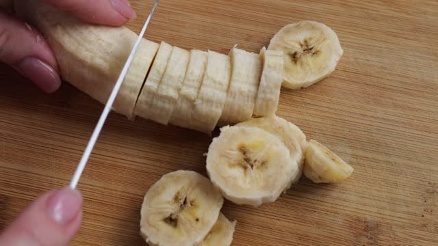 cut a banana on a wooden board with a knife. girl cutting banana
