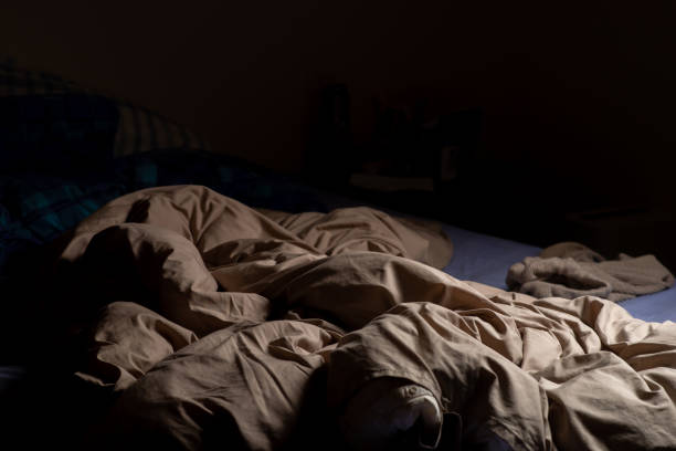istock An empty unmade bed in the dark. A crumpled blanket lit by a lamp. 1484259320