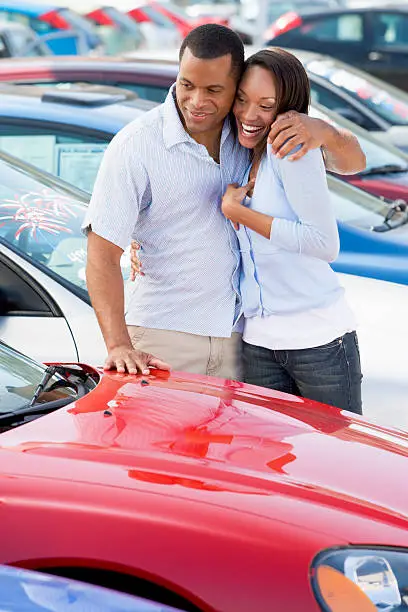 Young couple looking at new cars on car lot hugging and smiling