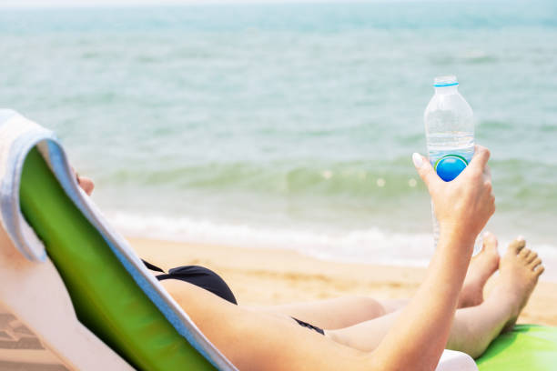 Woman drinking water and rests on a sunbed on the beach.