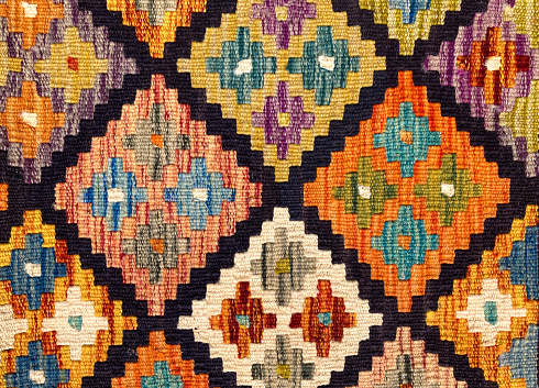 A close-up detail of an Afghan kilim rug  in orange, yellow, turquoise.