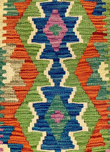 A close-up detail of an Afghan kilim rug  in blue, green and orange.
