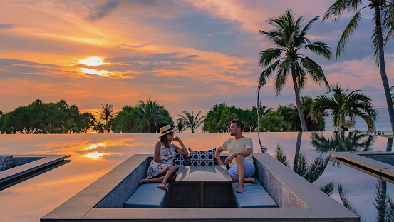 couple watching the sunset in an infinity pool on a luxury vacation in Thailand, man and woman watching the sunset on the edge of a pool in Thailand on a luxury vacation