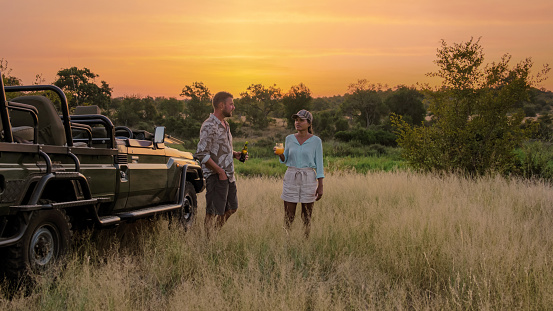 Asian women and European men on safari game drive in South Africa Kruger national park. a couple of men and women on safari watching the sunset. Tourists in a jeep looking sunset with drinks on safari