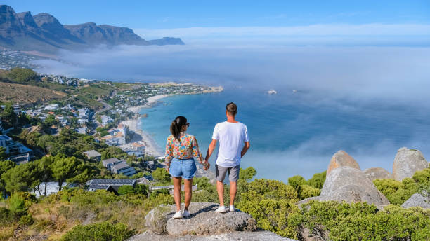 The Rock viewpoint in Cape Town, Camps Bay with fog over the ocean in Cape Town South Africa Couple at The Rock viewpoint in Cape Town Campsbay, view over Camps Bay with fog over the ocean. fog coming in from the ocean in Cape Town South Africa, men and women at a viewpoint table ledge stock pictures, royalty-free photos & images
