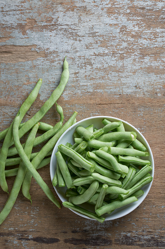 fresh green beans on white bowl, aka french beans, string beans or snaps, harvested vegetable on a rustic table top, taken straight from above with copy space