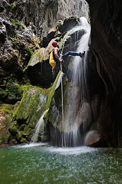 Extreme canyoning series. Male explorer rappeling down the waterfall deep in the mountains.