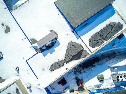 Elevated overhead drone view of a flat roofed building with snow load and ventilation units. High quality photo