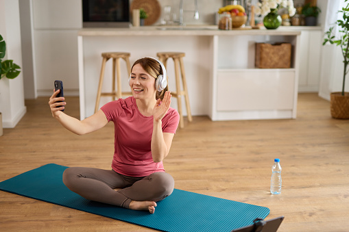 Young woman using cellphone and taking Selfie while exercising yoga at home