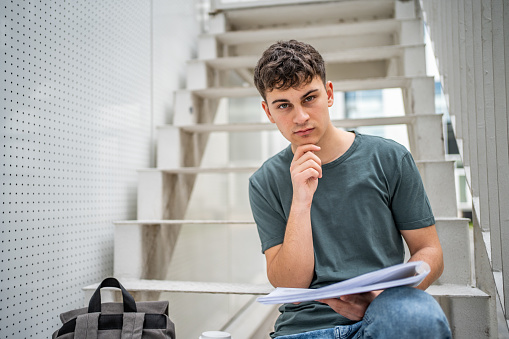 A high school student or student sits on the steps of his school building and studies