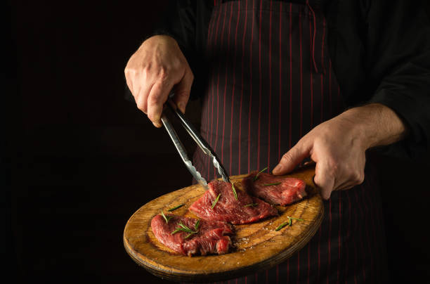 istock The cook holds a cutting board with raw beef steaks before barbecue. Preparation for roasting meat with rosemary and spices. Black space for restaurant recipe or hotel menu 1484308215