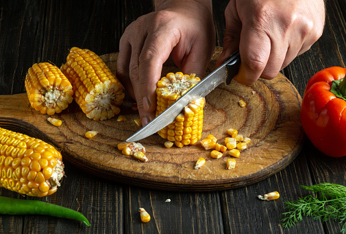 Chef cuts corn kernels with a knife. Maize is an excellent dietary breakfast or lunch by the cook hands. Space for recipe or menu