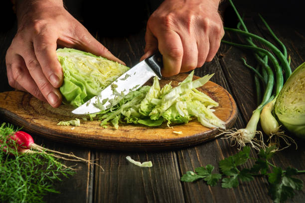 istock Slicing cabbage on a cutting board. Delicious salad for dinner with fresh vegetables. Hands of a chef with a knife while cooking in a kitchen. 1484310364