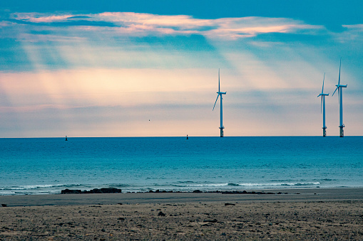 Aerial drone view of a wind turbine in the foreground of a coal fired power generating station.