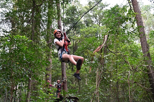 Teenager girl (female age 12) sliding on a flying fox zip line during a treetop adventure climbing. Girls power, risk and challenge concept. Real people. Copy space