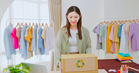 asian female fashion clothing designer is packing commodity with reusable carton