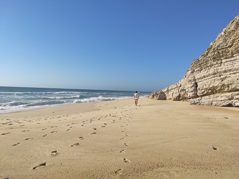 Boy walking throw the sand beach, far away.