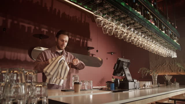 Barman arranging wine glasses hanging above counter