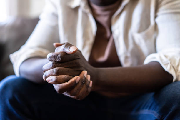 Close up of a pair of hands clasped together Close up of an unknown African-American man's claspling hands with the elbows leaning on his knees men hands stock pictures, royalty-free photos & images