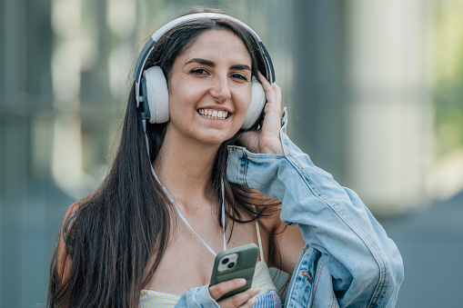 girl on the street listening to music with headphones and mobile phone or smartphone