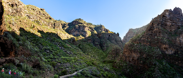 Hikers on a mysterious adventure through the lush greenery and rocky cliffs of Barranco del infierno ravine, Hell's gorge, in Adeje Tenerife, in the tranquil atmosphere and beauty of the idyllic path.