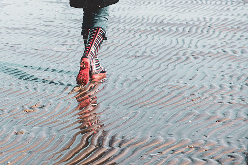 Partial view of a person walking through the Wadden Sea in rubber boots at low tide
