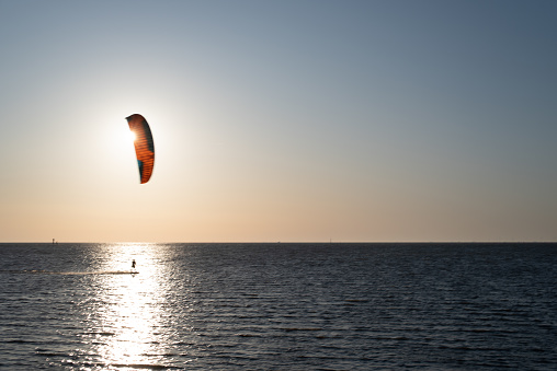 Backlit shot of a kitesurfer in front of the rising sun