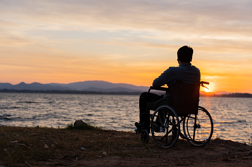 Man sitting on wheelchair with first golden sunrise of the day. Disabled handicapped people with hope.