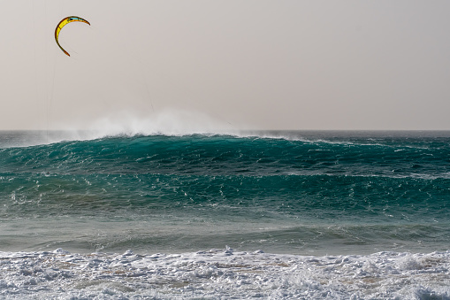 strong waves on the beach with kite sails in the background