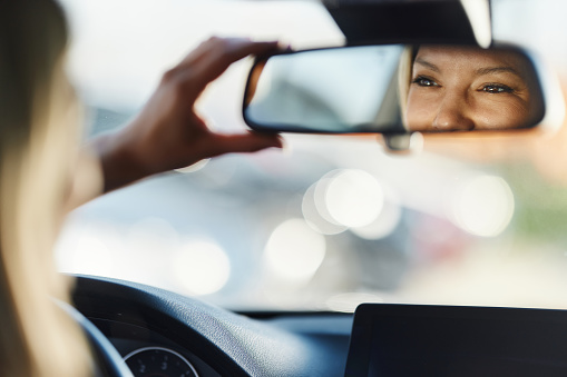 Close up reflection of happy woman adjusting her rear-view mirror in a car.