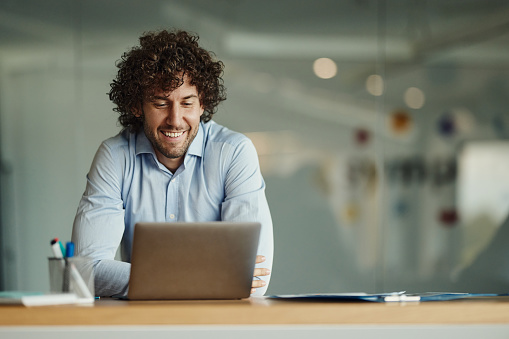 Young happy businessman reading an e-mail on a computer in the office. Copy space.