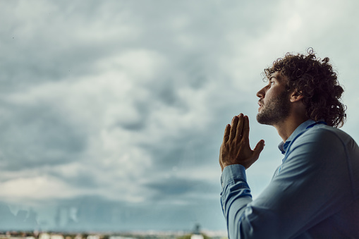 Young male entrepreneur praying against the sky. Copy space.