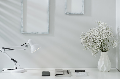 Planner, smartphone and calculator under lamp on white office desk