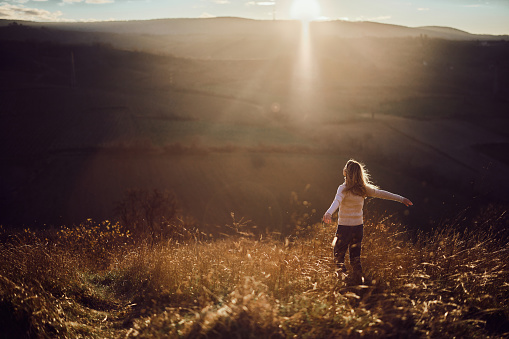 Back view of carefree woman with her arms outstretched on a hill in autumn day at sunset. Copy space.